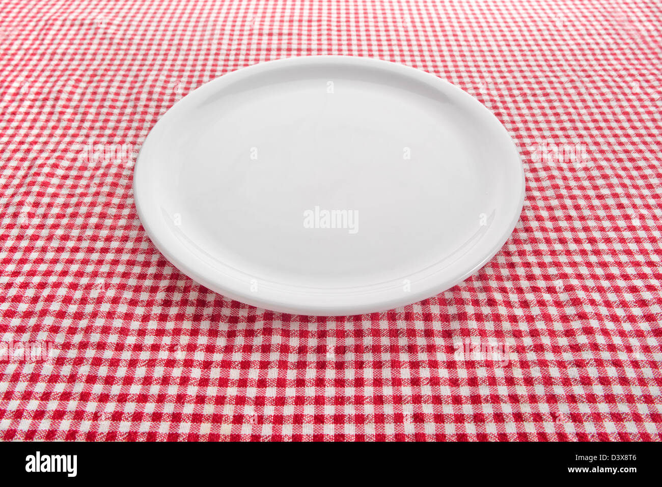 Leere weiße Platte am Küchentisch mit karierten Tischdecke bedeckt. Stockfoto
