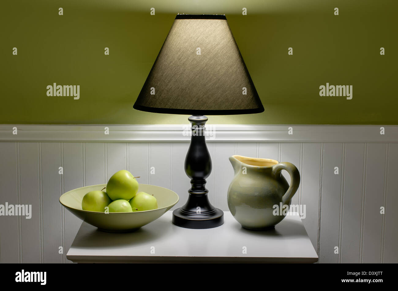 Schüssel mit grünen Äpfeln, Lampe und Krug auf den Tisch. Szene wird nur durch weiches Licht aus Lampe beleuchtet. Stockfoto