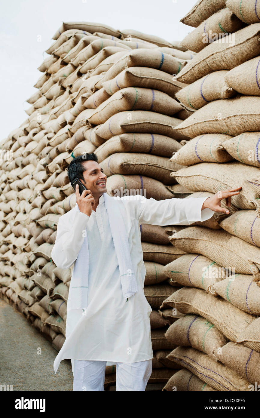 Mann stand in der Nähe Säcke Weizen und sprechen auf einem Handy Anaj Mandi, Kapur, Gurgaon, Haryana, Indien Stockfoto