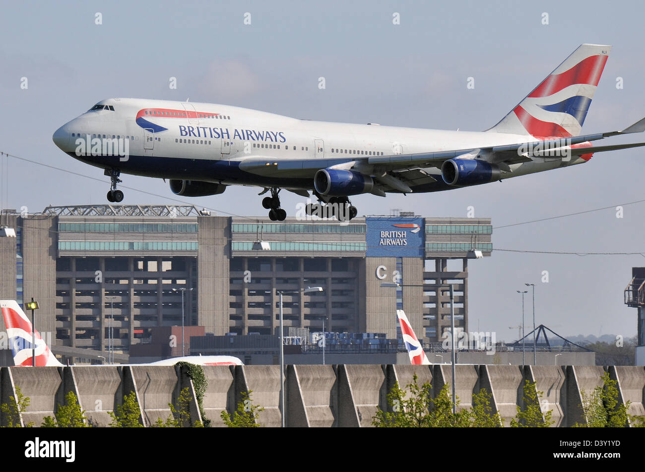 British Airways 747, das in Heathrow landet, überquert den Wartungshangar der British Airways mit anderen BA-Flugzeughängen Stockfoto