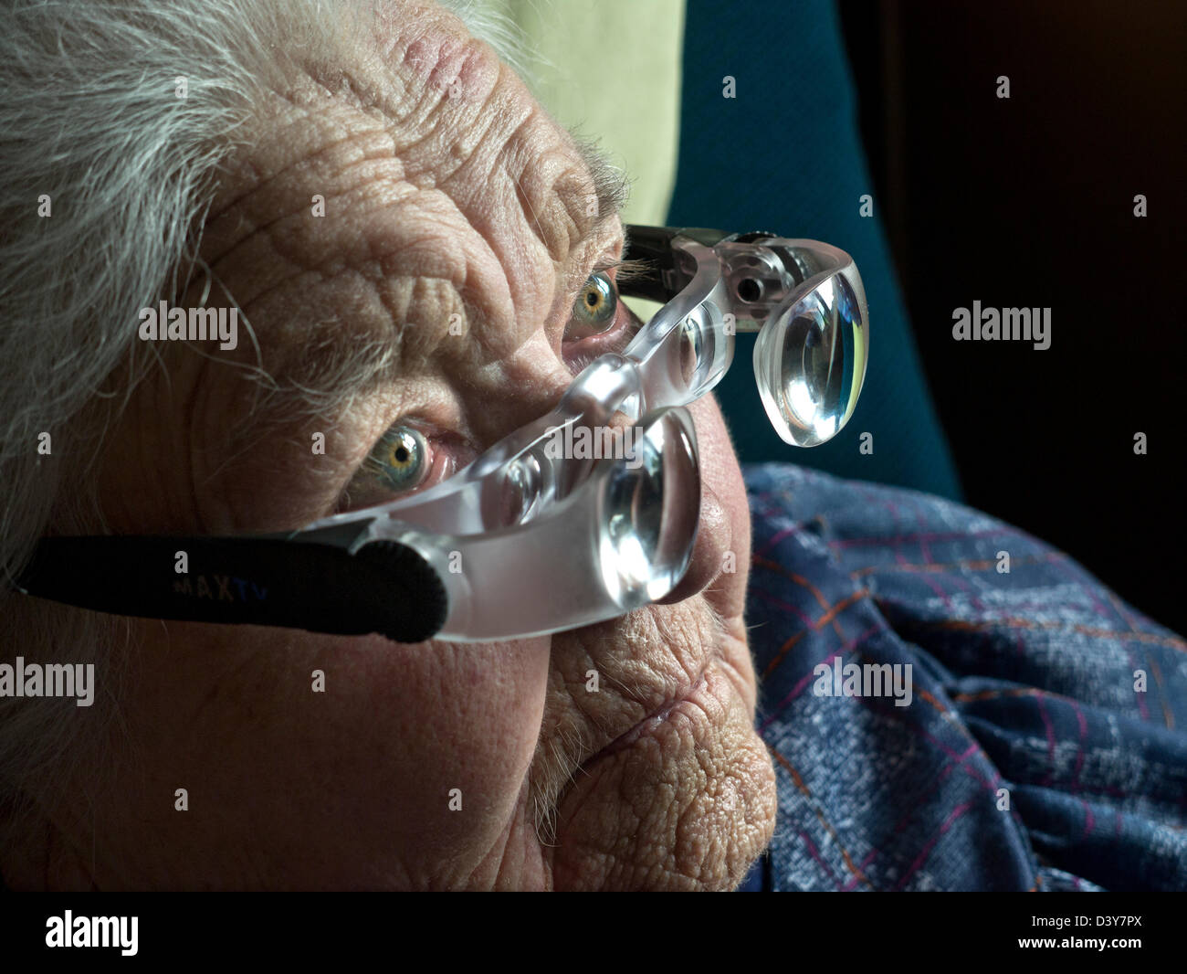 Makuladegeneration ältere alte ältere Dame mit Sehbehinderung Auge Sehkraft trägt spezielle Vergrößerungsgläser, um in ihr Fernsehen zu sehen Zimmer Stockfoto