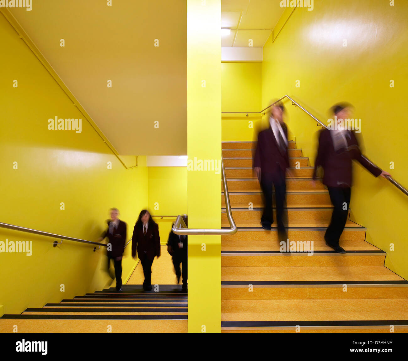 RSA-Akademie, Tipton, Vereinigtes Königreich. Architekt: John McAslan & Partner, 2011. Leuchtend gelbe Treppe mit Studenten in Bewegung. Stockfoto