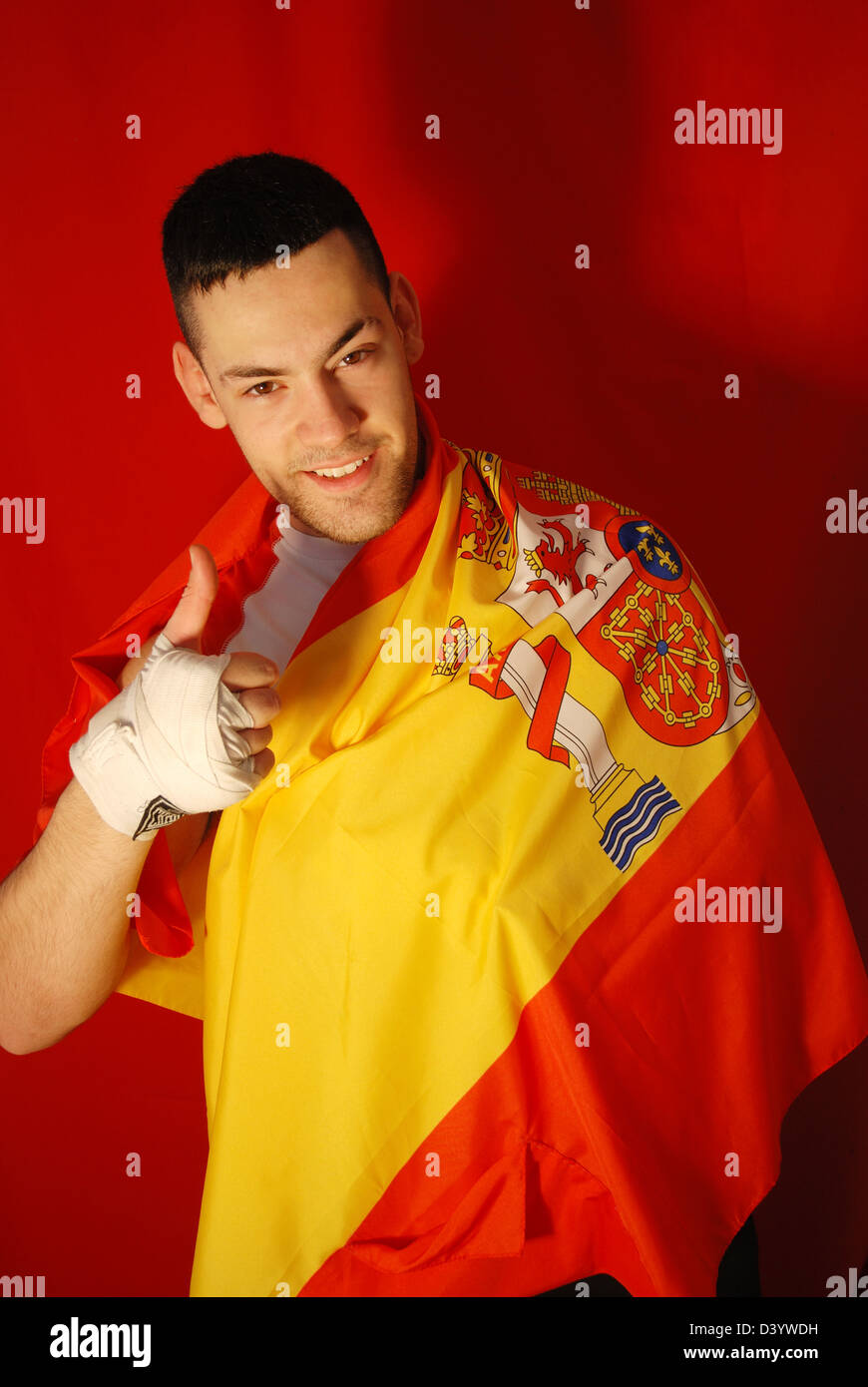 Junger Mann eingewickelt in eine spanische Flagge, lächelnd und Daumen nach oben. Stockfoto