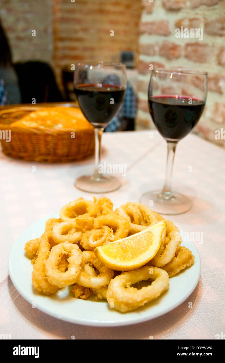 Spanische Vorspeise: gebratene Tintenfische mit zwei Gläser Rotwein servieren. Madrid, Spanien. Stockfoto