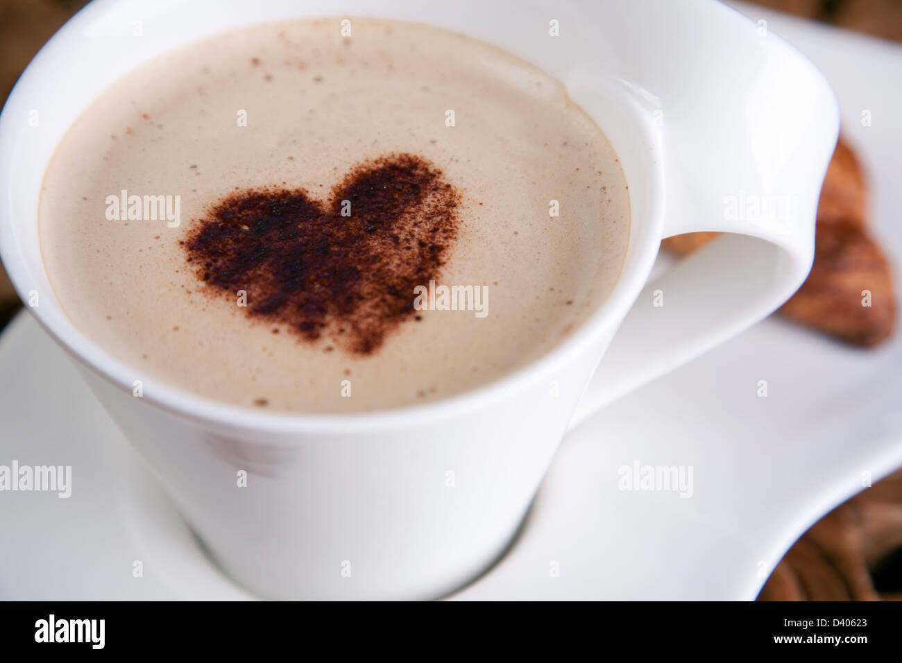 Ein schicker Kaffee Latte mit einer Liebe Herzen an der Spitze in einem sauberen leuchtend weißen Tasse Becher mit kleinem von konzentrieren Dänisch seitlich Stockfoto