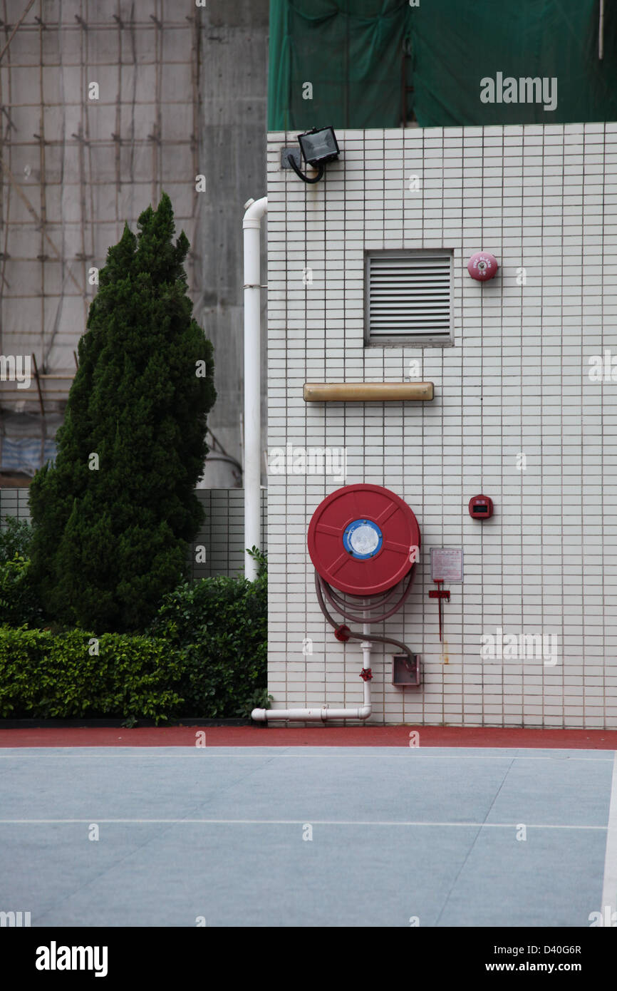 Es ist ein Foto von einem Feuer Hacke oder Hydranten, die gegen eine Wand aus Fliesen in der Nähe ein Tennis-Spielplatz. Wir können einen Baum sehen. Stockfoto