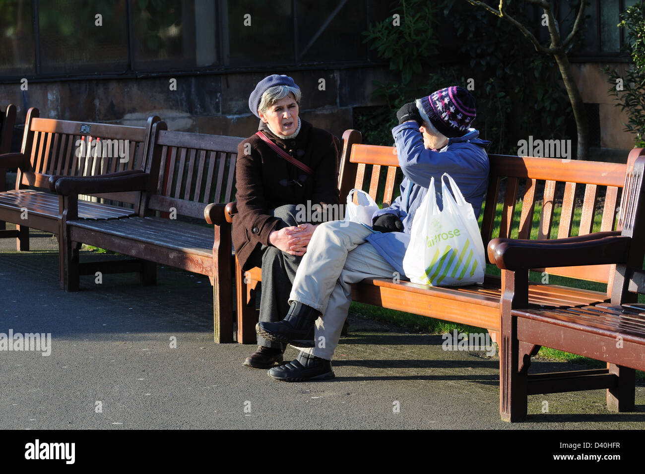 Zwei Frauen machen Sie eine Pause vom einkaufen sitzen sprechen in einem lokalen Park, Glasgow, Schottland, Großbritannien Stockfoto