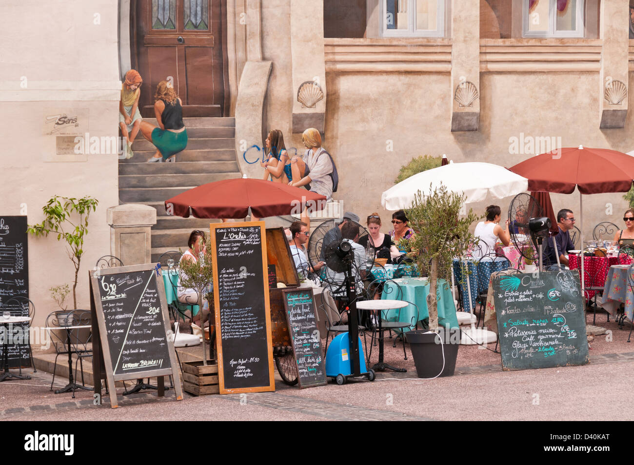 Menschen mit Mittagessen im Außenrestaurant mit Wandbild im Hintergrund, Montpellier, Hérault, Languedoc-Roussillon, Frankreich Stockfoto