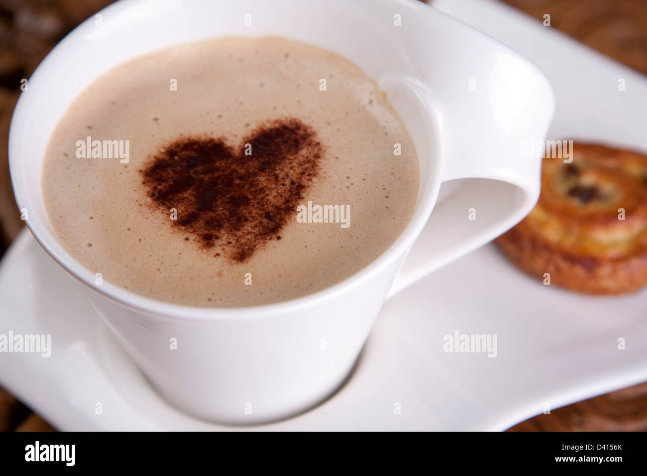 eine Tasse Becher Kaffee Latte mit einer Liebe Herz Schokolade bestreuen an der Spitze und einem dänischen auf der Seite Stockfoto