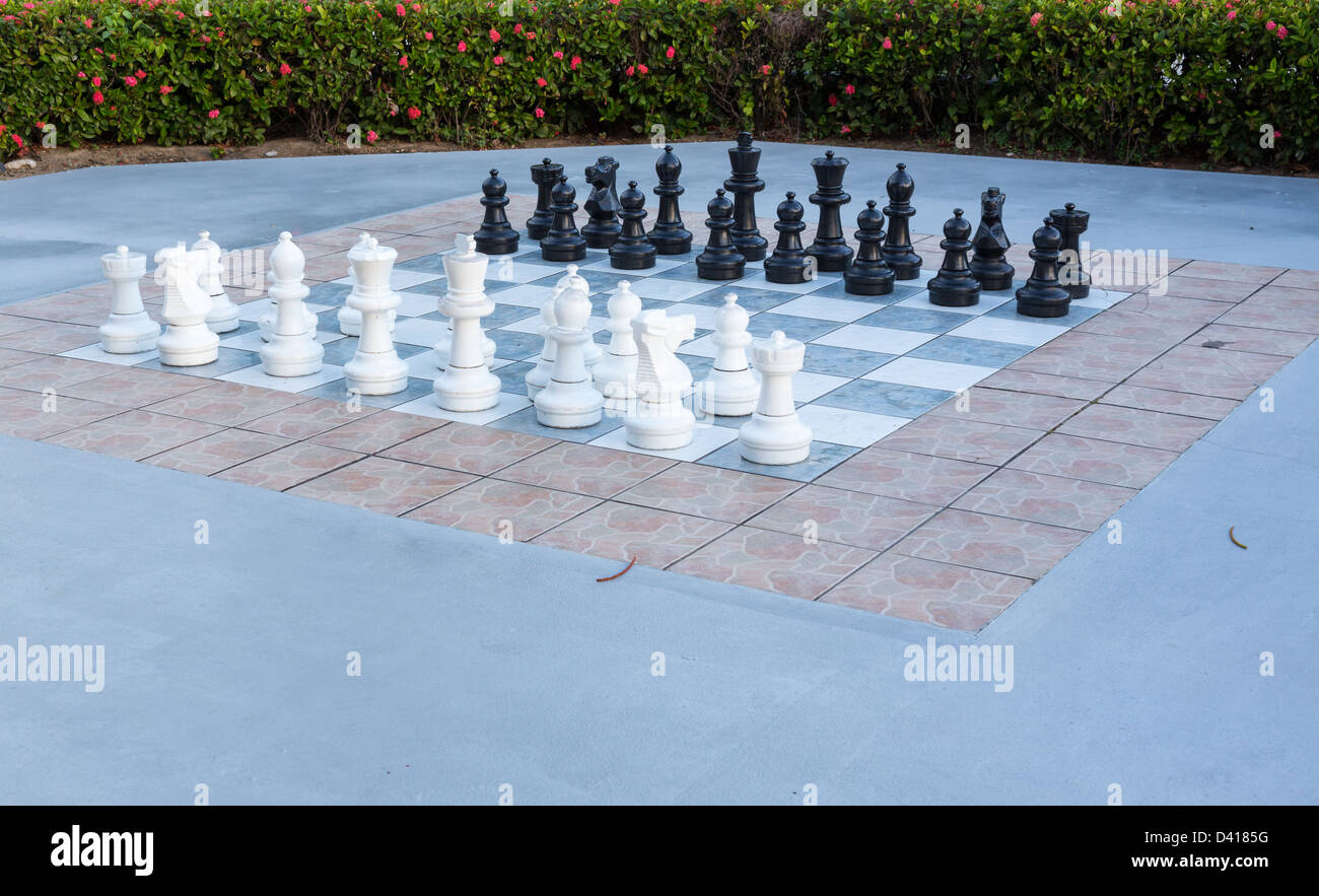 Große weiße und schwarze Stücke in Outdoor-Schachspiel im Blumengarten Stockfoto