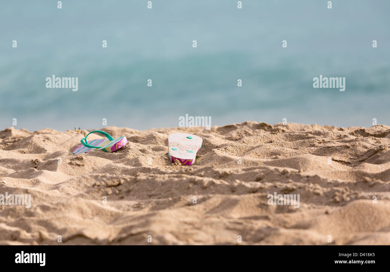 Ausrangierte Childs Flip-Flops am Sandstrand vom türkisblauen Ozean in Sonne Stockfoto