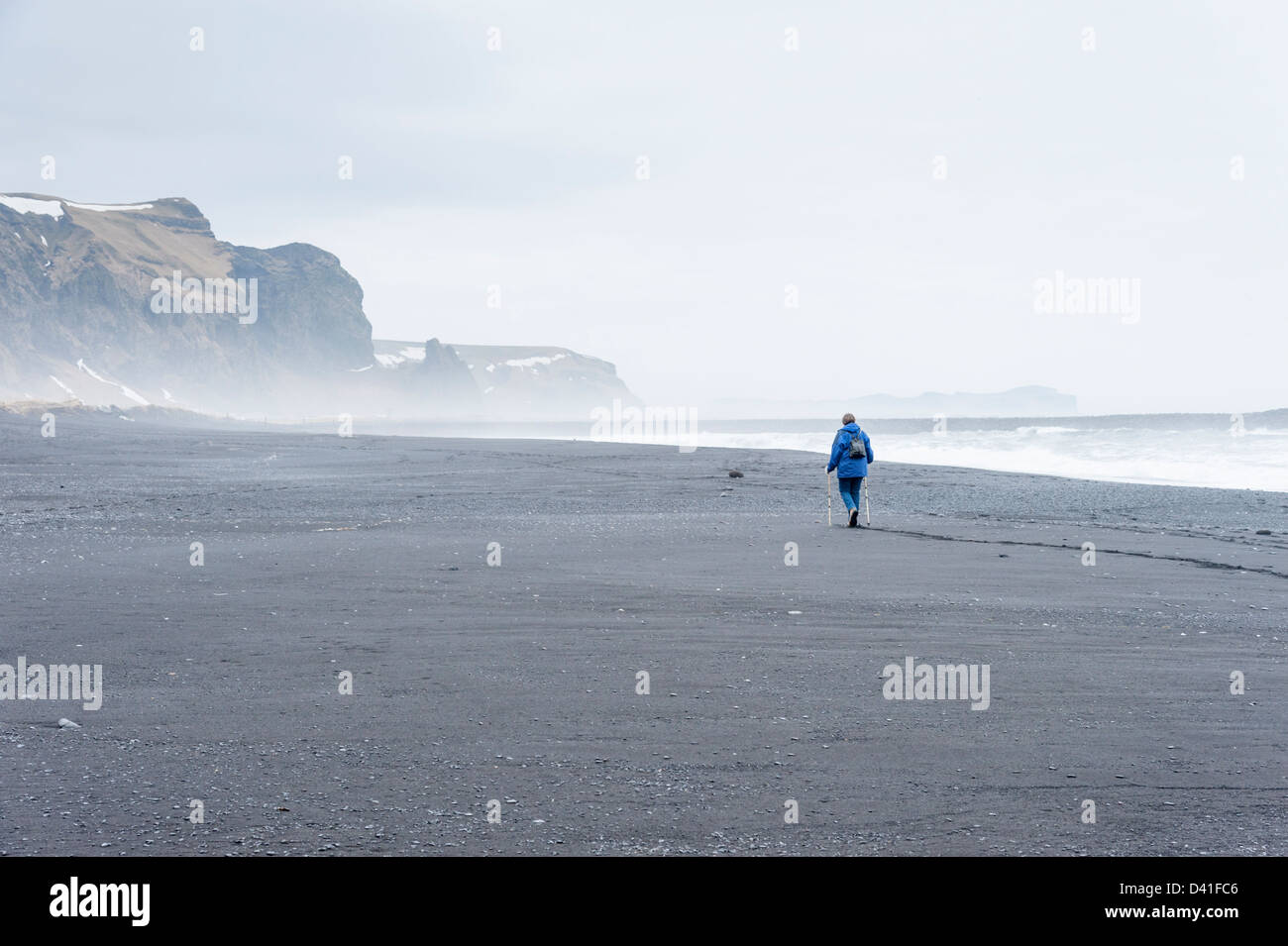 Eine einsame Person, die zu Fuß auf den schwarzen vulkanischen Sandstrand bei Vík Í Mýrdal Island Stockfoto