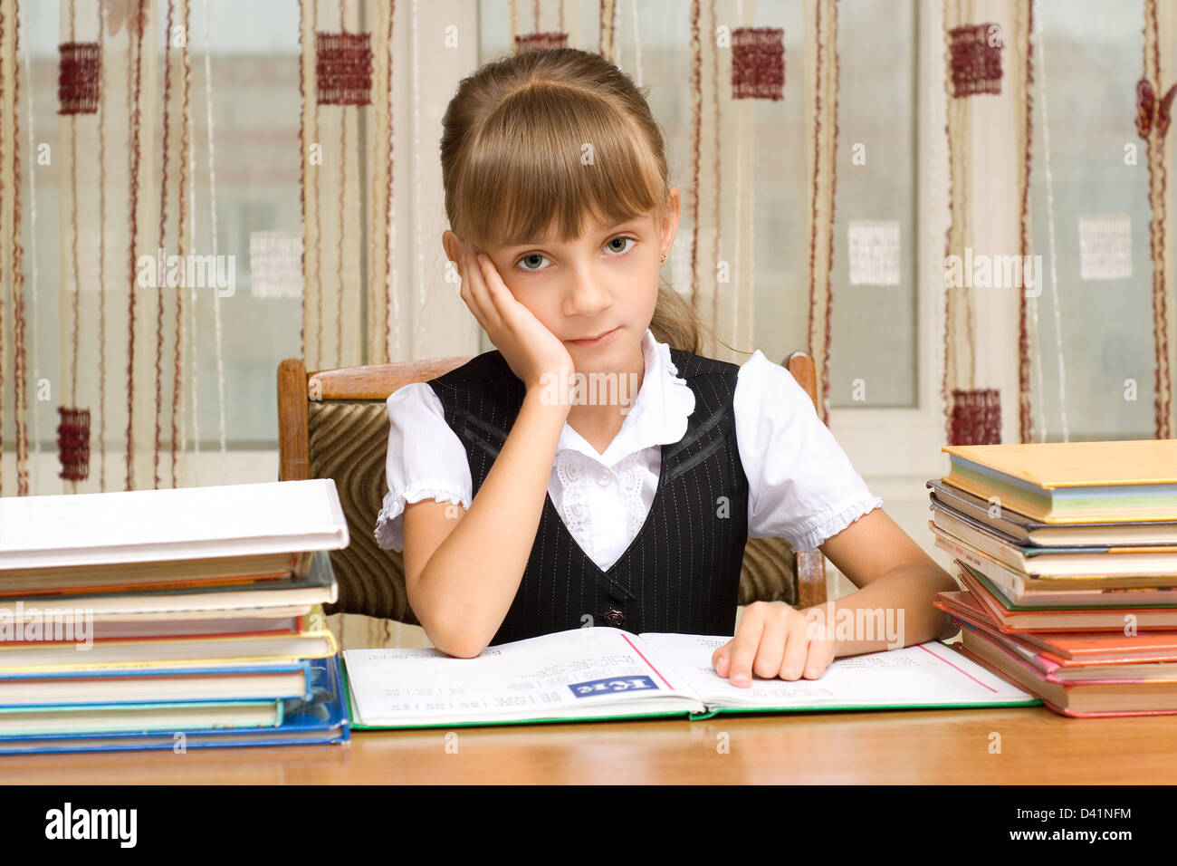 Die müde Schülerin sitzt an einem Tisch mit Büchern Stockfoto