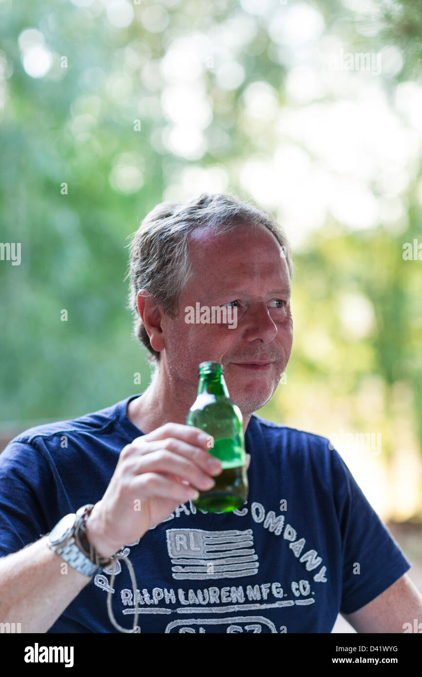 An einem heißen Sommertag entspannt ein Mann draußen im Schatten durch das Trinken einer Flasche Bier. Stockfoto