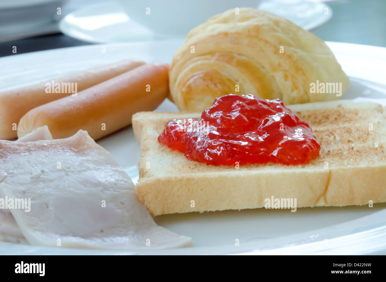 Frühstück am weißen Teller (Speck, Brot, Wurst, Toast und Marmelade) Stockfoto