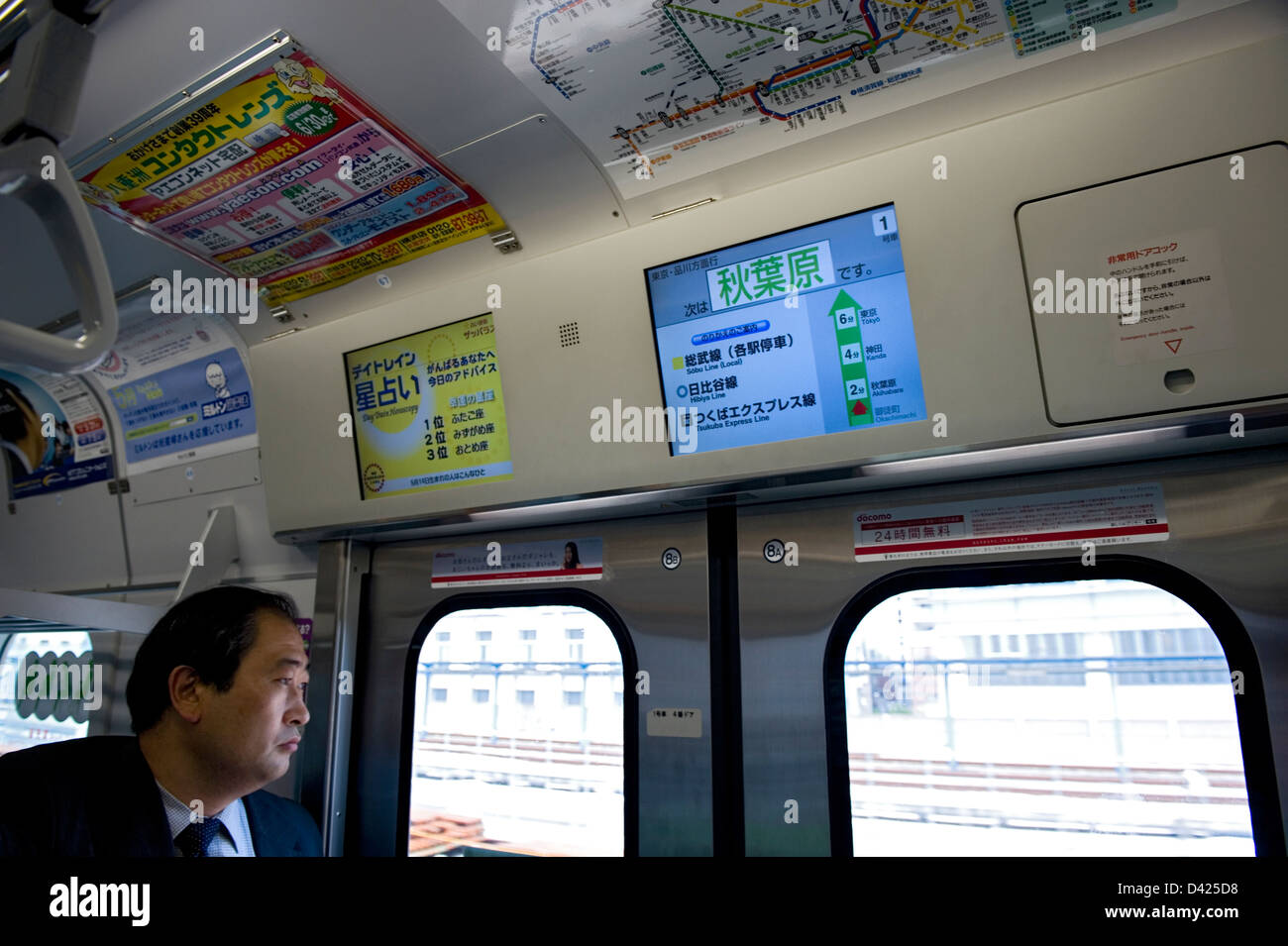 Unternehmer-Kollegen aus Fenster von Tokios Yamanote Loop Line-Zug. Nächster Halt ist Akihabara, wie auf TV-Monitor angezeigt. Stockfoto