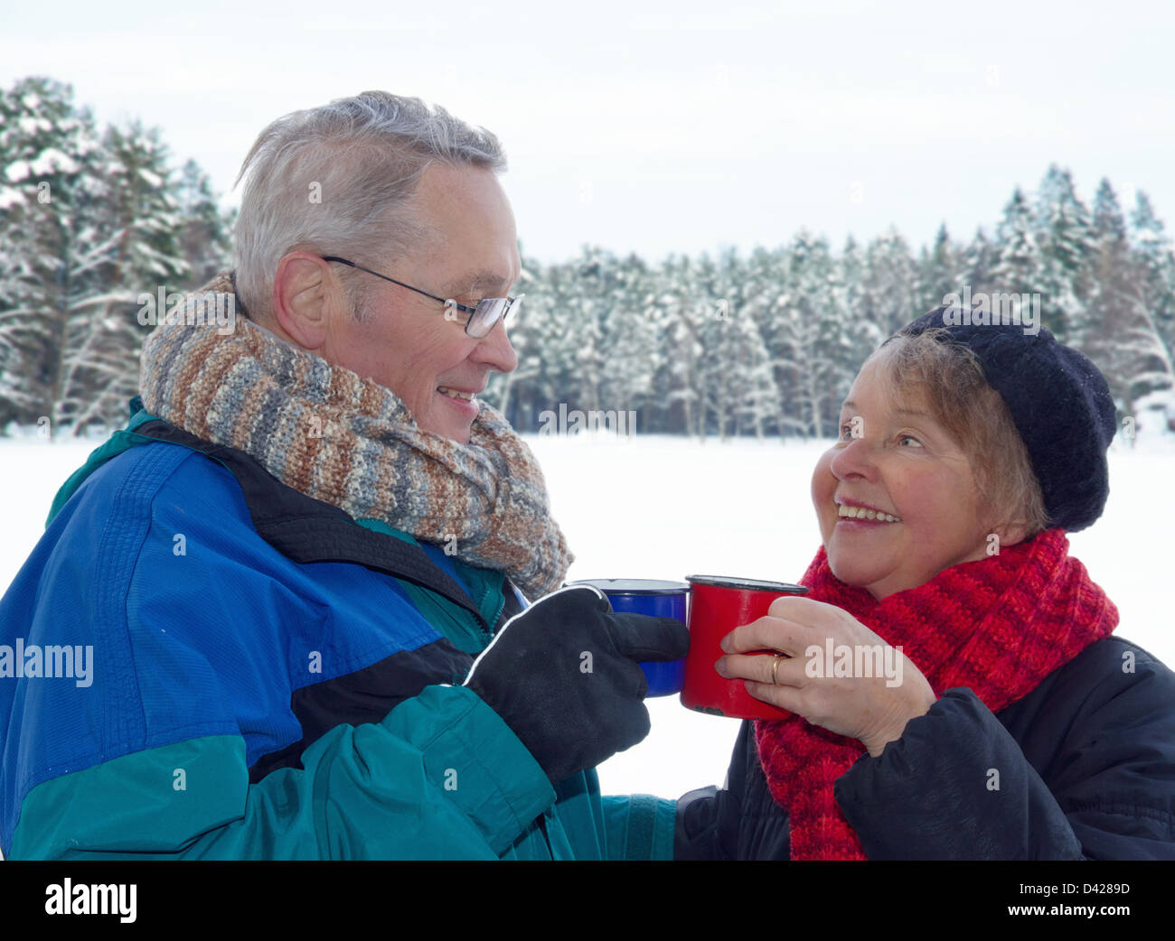 Ältere glückliche Paar Toasten mit Tassen warmen Getränke, draußen im Schnee Winter Waldlandschaft Stockfoto