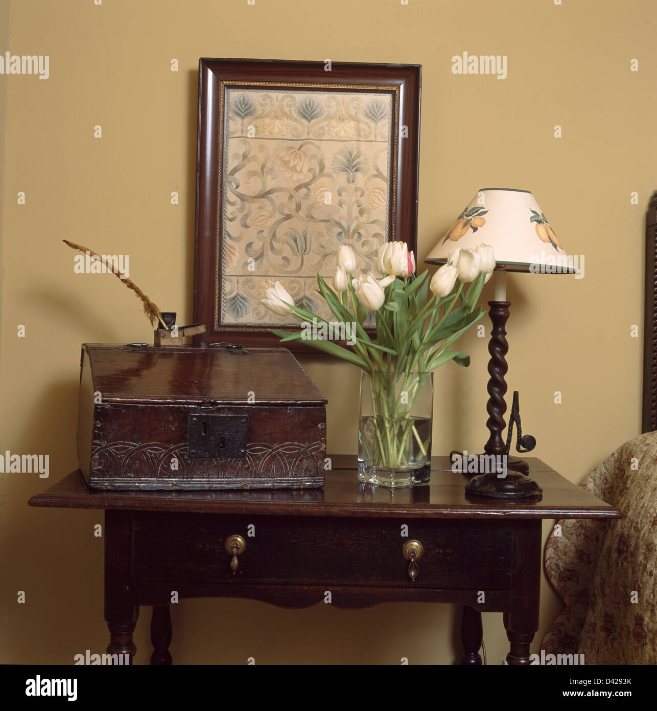 Antike Box mit weißen Tulpen und hölzerne Lampe auf antiken Holztisch Konsole unter eingerahmte Stickerei Bild Stockfoto