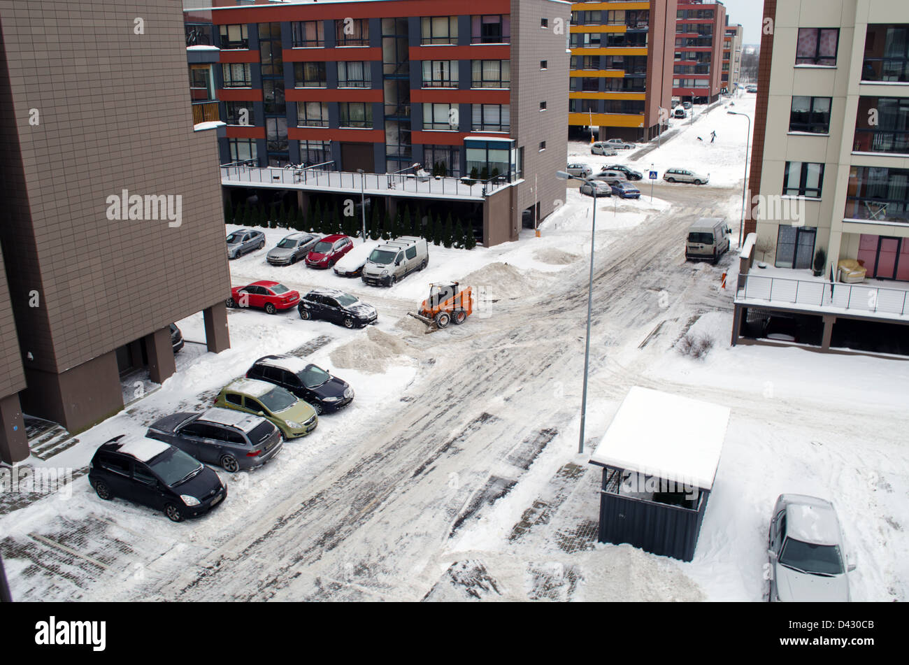 kleiner Traktor Bagger Bobcat arbeiten sauber Schnee in der Nähe von flachen Blockhäuser Parkplätze an der Straße. Stockfoto