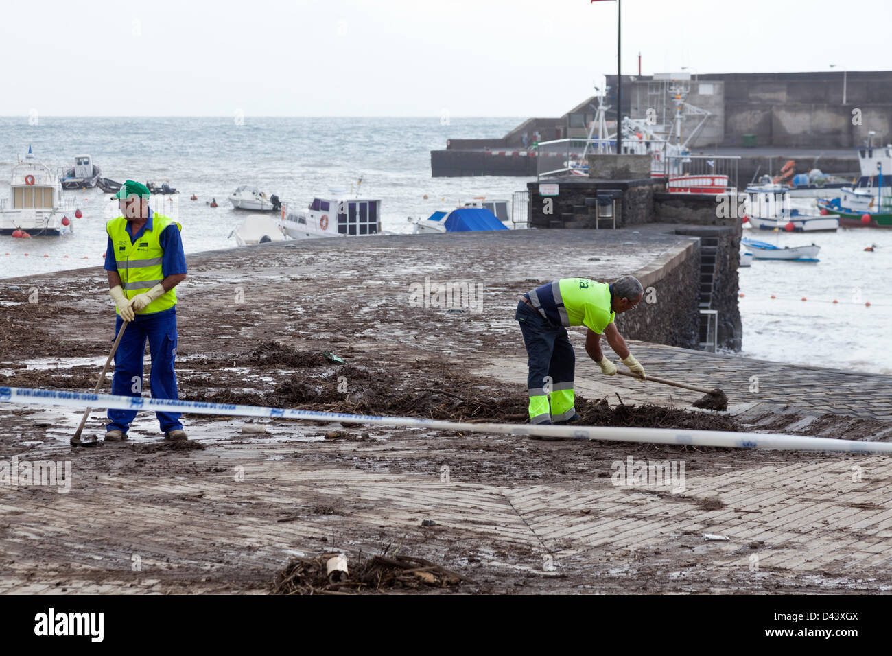 Aufräumarbeiten nach Sturmschäden in Playa de San Juan, Guia de Isora, Teneriffa, Kanarische Inseln. Windgeschwindigkeiten von bis zu 100 km/h und extrem starke Regenfälle verursachten Überschwemmungen bringen viel Schlamm und andere Verunreinigungen an der Strandpromenade und Gehwege von San Juan. Stockfoto