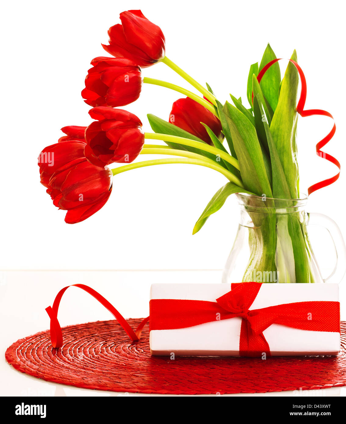 Bild der schönen roten frischen Tulpen Blumen in Glas Vase, weißen Geschenkbox mit roter Schleife auf dem Tisch im Studio, Stockfoto