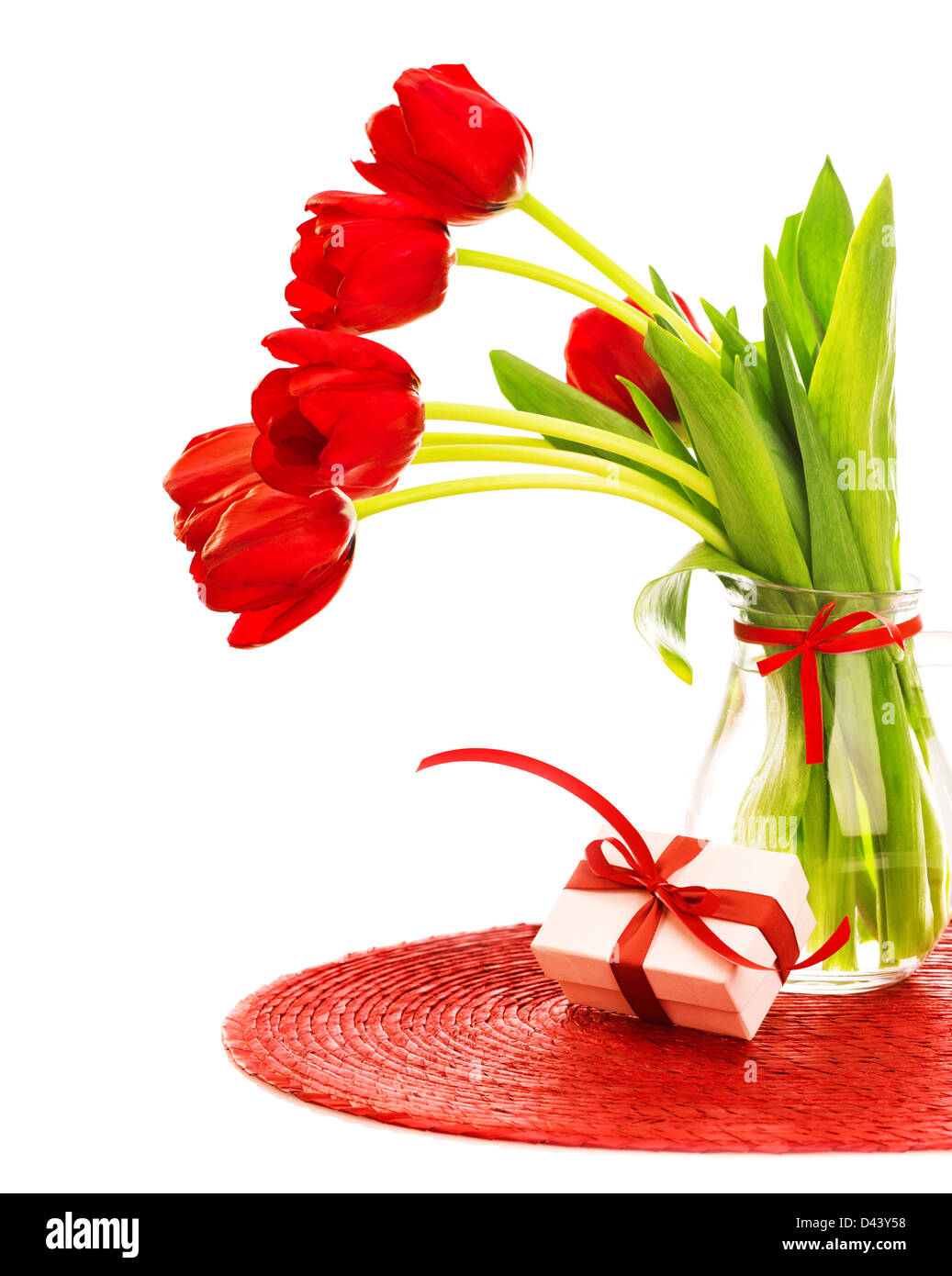Foto von schönen roten frischen Tulpen Blumen in Glas Vase, weißen Geschenkbox mit roter Schleife auf dem Tisch im Studio, Stockfoto