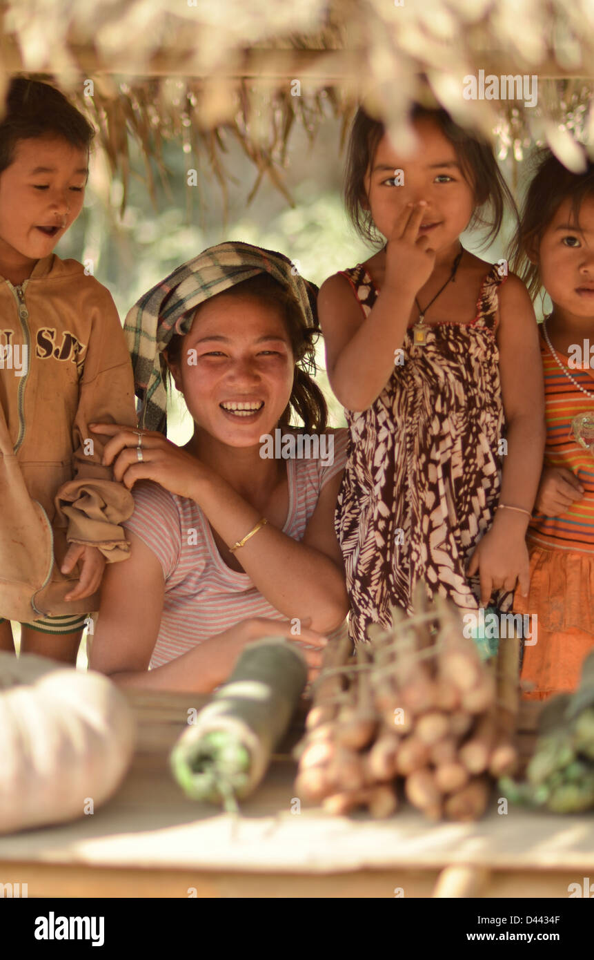 Drei Kinder und eine junge Frau, Verkauf von Gemüse von einem Straßenrand in Laos Stockfoto