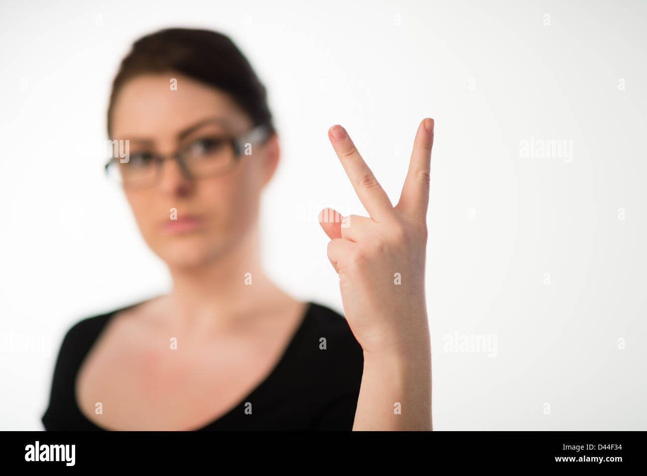 Eine junge Frau, braune Haare, zwei Finger V Zeichen-Finger-Geste beleidigen Beleidigung UK Stockfoto