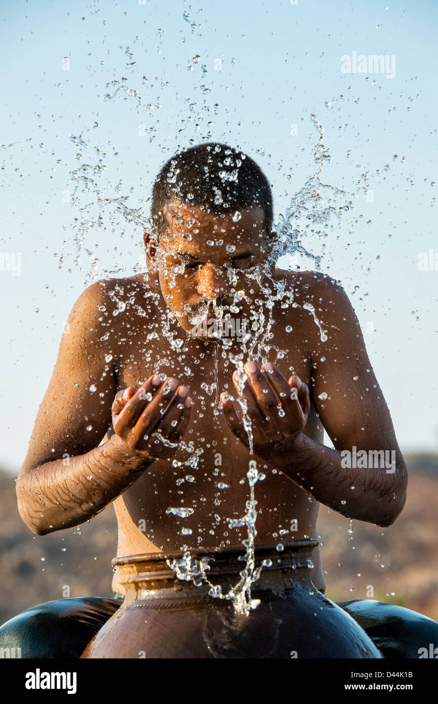 Indischer Mann Spritzwasser über sich selbst aus einem Wassertopf bei Sonnenuntergang. Indien Stockfoto