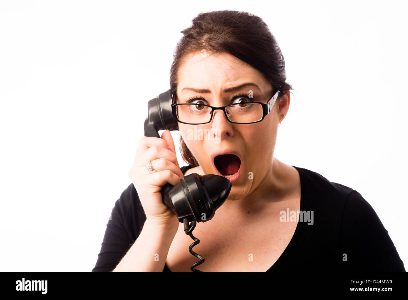 Eine junge Frau schockiert braune Haare suchen, hält eine altmodisches Telefon, UK Stockfoto