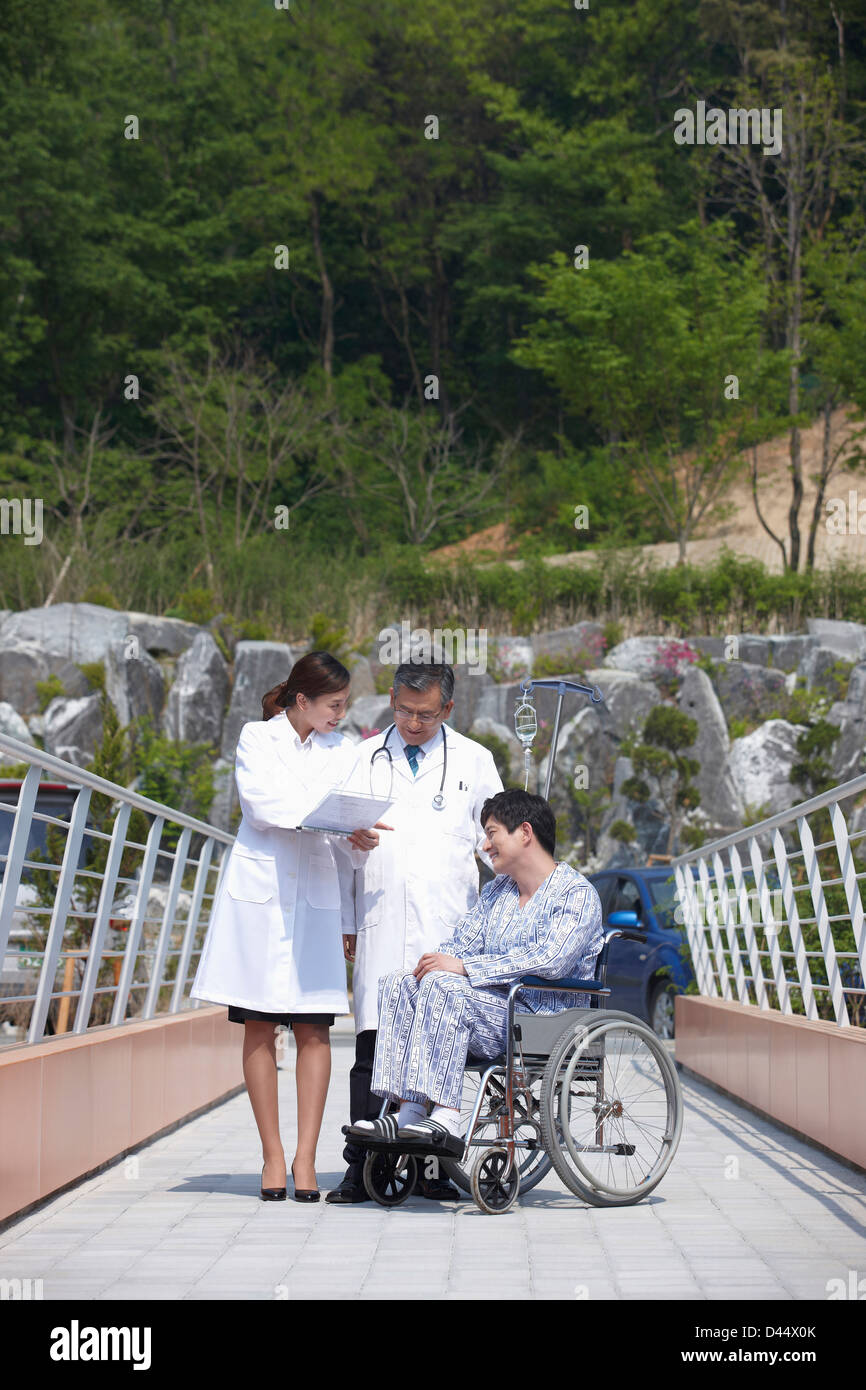 ein Patient im Rollstuhl und Ärzte, die Überprüfung der Papiere auf einer Brücke Stockfoto