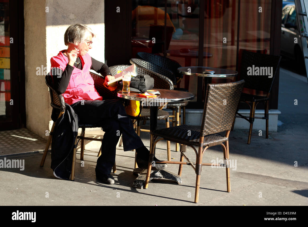 Ältere Frau im sonnigen Outdoor Café in Paris sitzen, ein Buch zu lesen und Rauchen Stockfoto