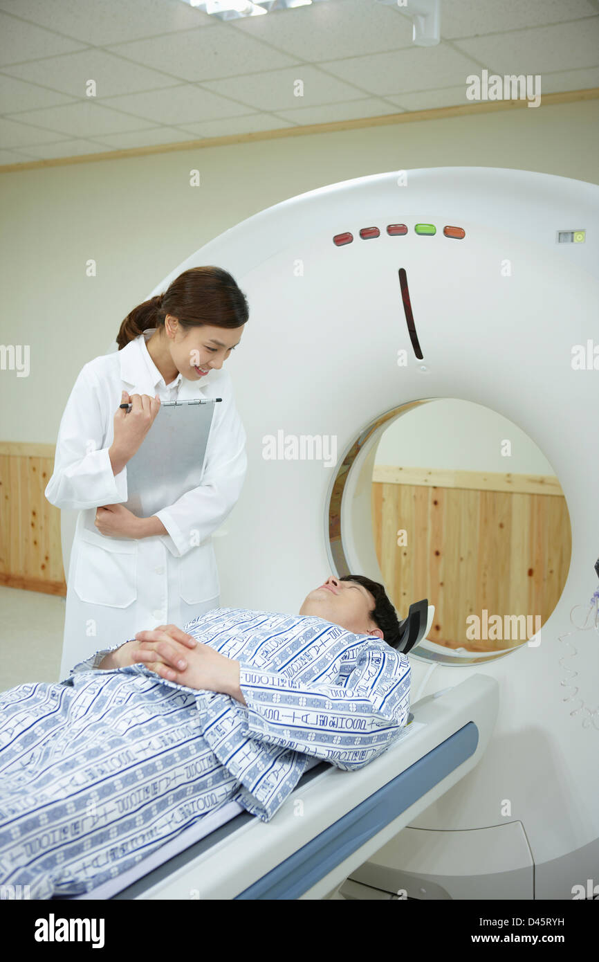 ein Arzt steht neben einem Patienten auf CT-Scannerbett liegend Stockfoto