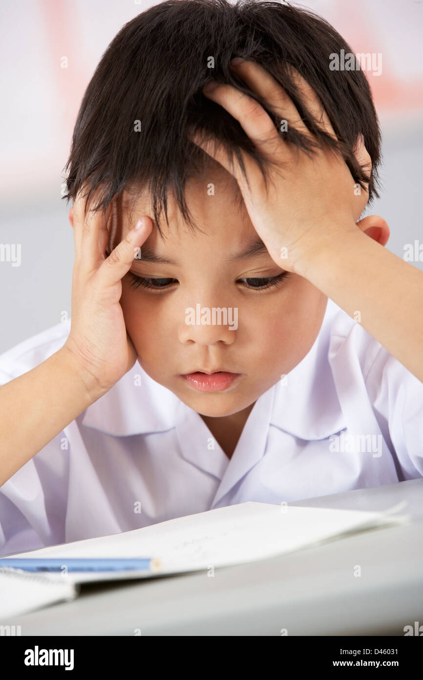 Unglückliche männlichen Studenten, die Arbeiten am Schreibtisch In Chinesisch Schule Unterricht Stockfoto