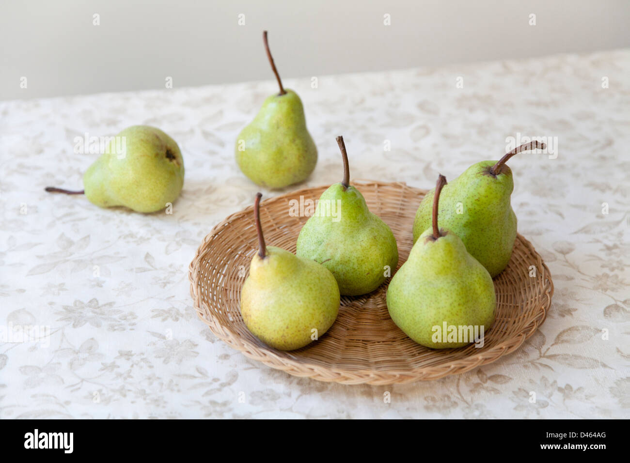 Sechs grüne Birnen auf einem geflochtenen Rattan Teller setzen auf eine leichte gemusterten Tischdecke Stockfoto