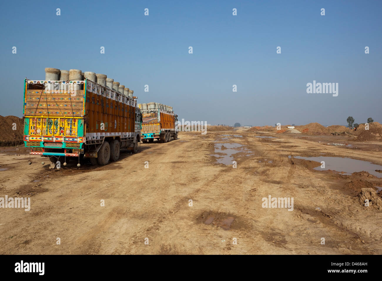 Hoch dekoriert Lastwagen voller Rohre warten auf neu geräumten ehemaligen landwirtschaftlichen Flächen am Stadtrand von Mohali in Punjab. Stockfoto