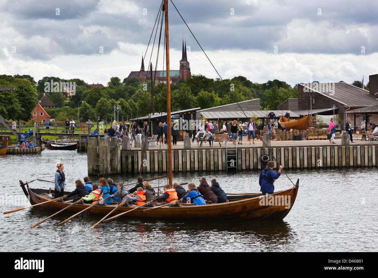 Touristen, die Rudern Viking Alter Schiff Replik auf das Wikingerschiff-Museum mit der Domkirke hinter Stockfoto