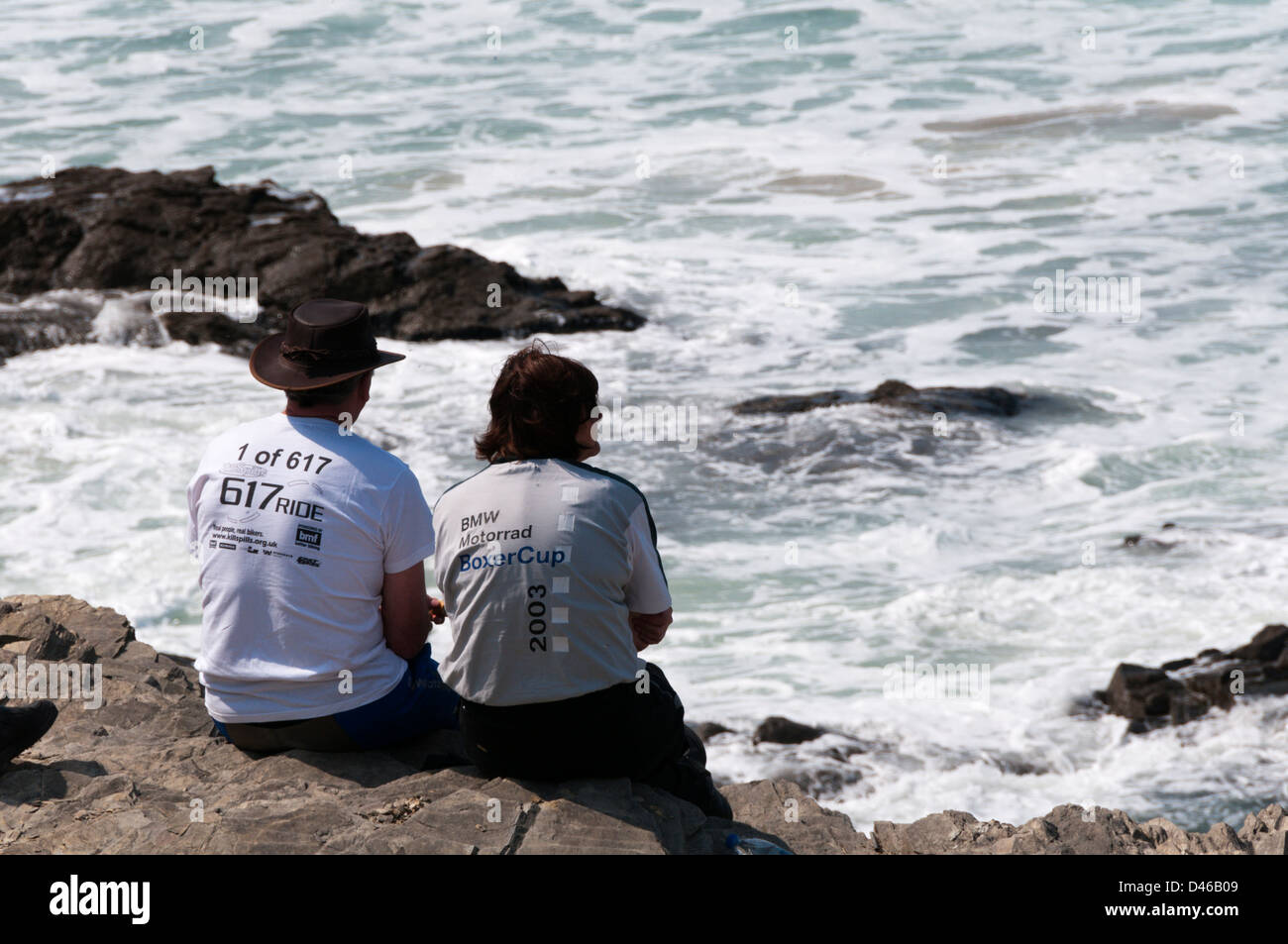 Ein paar mittleren Alters Biker sitzen auf Felsen, Wellen an der Nordküste Cornwalls zu beobachten. Stockfoto