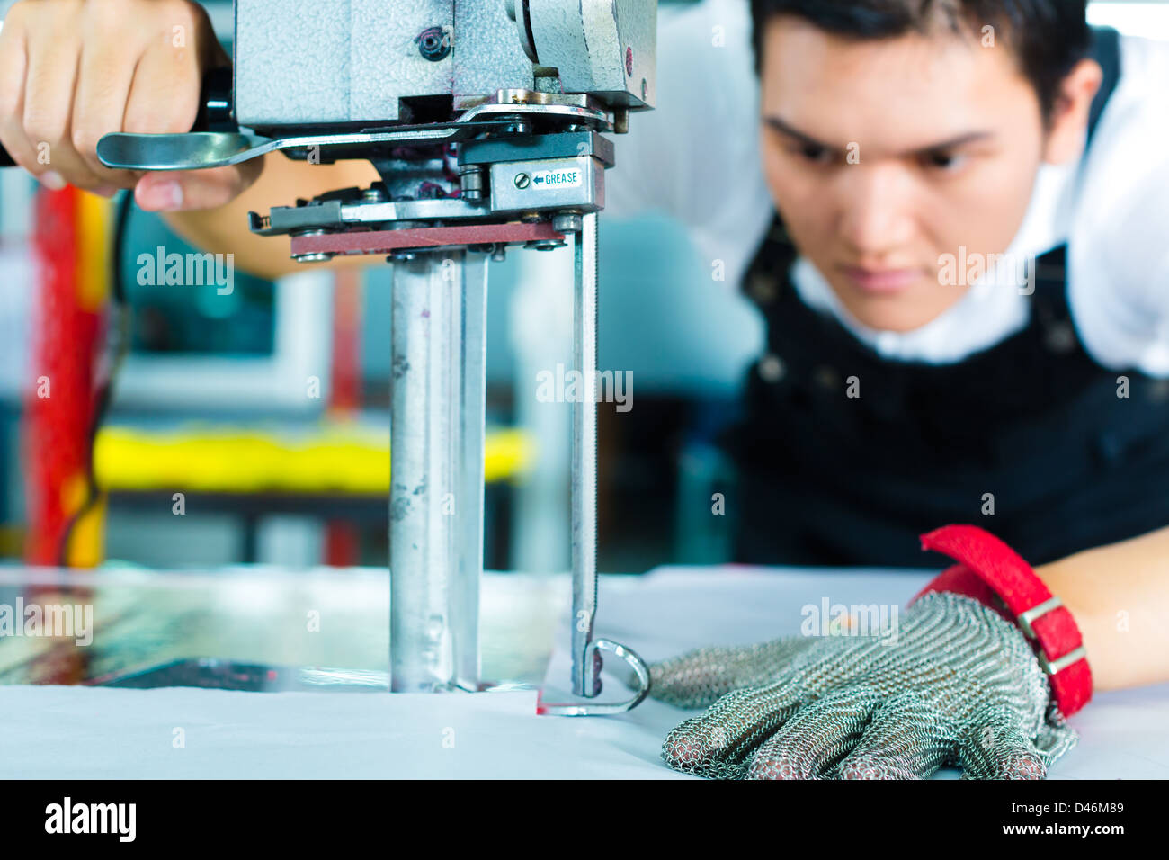 Arbeitnehmer mit einem Cutter - eine große Maschine für Schneiden Stoffe - in einer chinesischen Textilfabrik, He trägt angegossen Kette Stockfoto