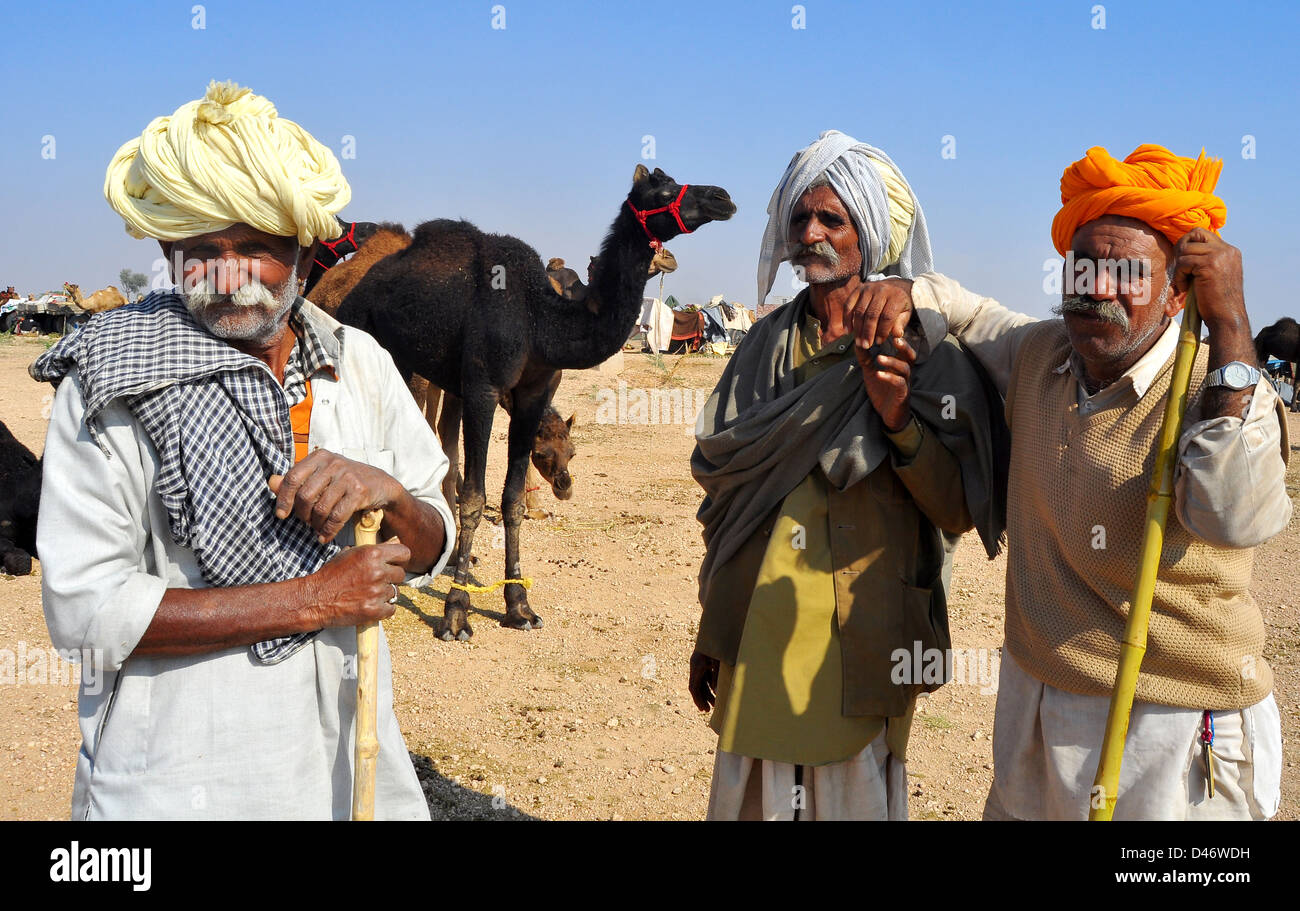 Kamel Händler lehnt sich auf ihrem Stick wie sie Uhren Kamele in der Nähe in einem Feld auf dem Kamel Messegelände in Nagaur, Staat Rajasthan. Stockfoto