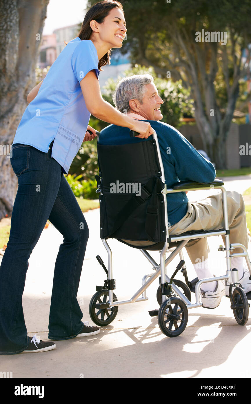 Pflegeperson Senior Mann im Rollstuhl schieben Stockfoto