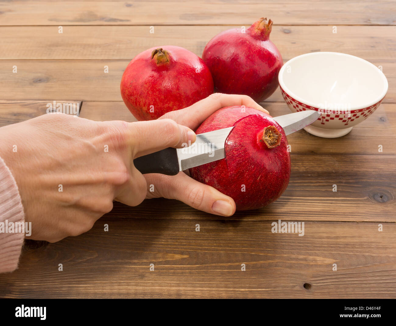Weibliche Hände schneiden einen frischen Granatapfel in Abschnitte Stockfoto