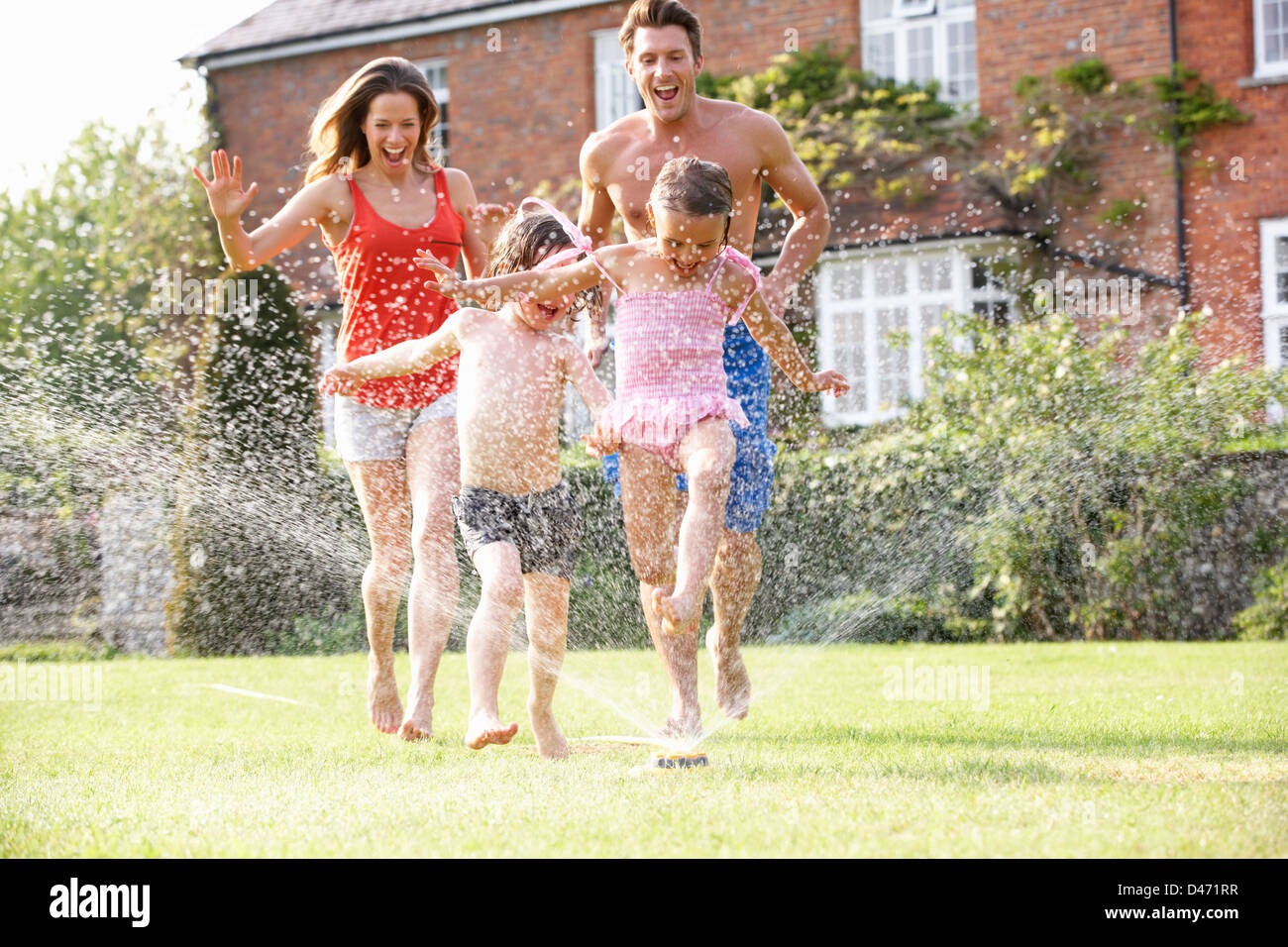 Familie durch Garten Sprinkler Stockfoto