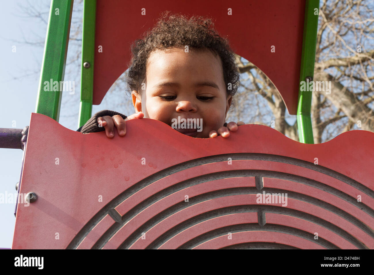 Gemischte Rassen Kleinkind Baby Lächeln und spielen am Klettergerüst an einem sonnigen Tag über Oberseite der Wand guckend Stockfoto
