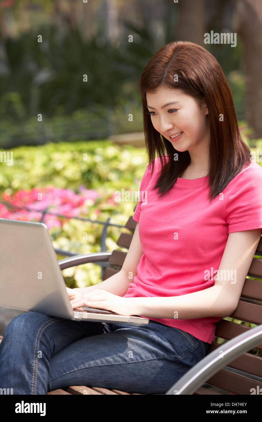 Junge Chinesin mit Laptop, während, entspannend auf Parkbank Stockfoto