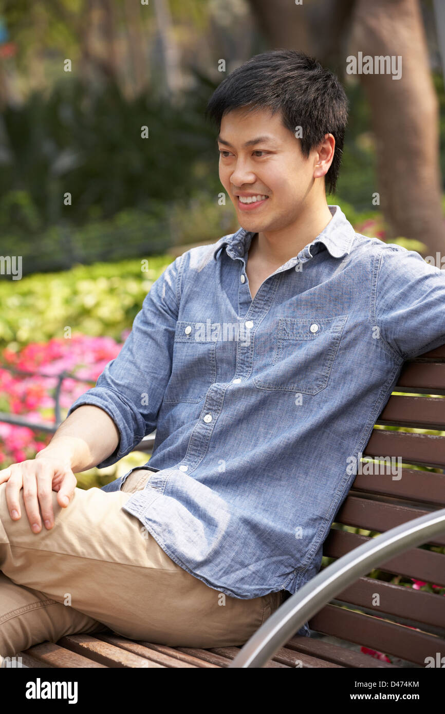 Junge chinesische Mann entspannend auf Parkbank Stockfoto