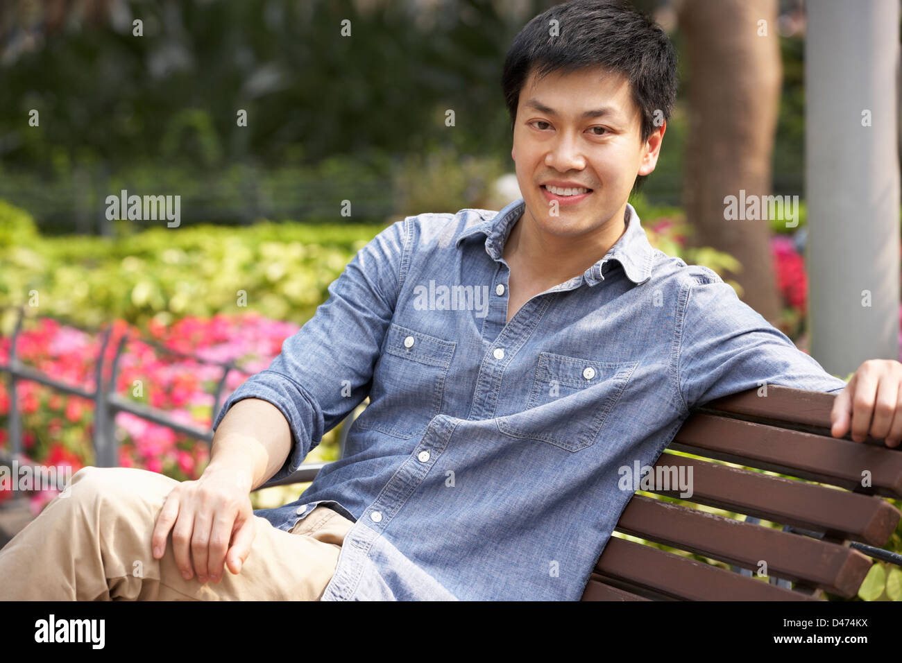 Junge chinesische Mann entspannend auf Parkbank Stockfoto