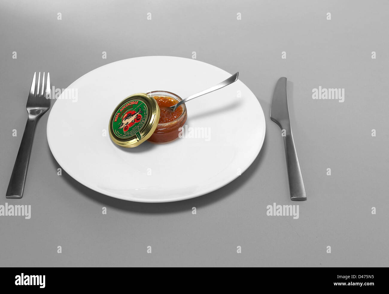 Topf mit Kaviar auf weißen Teller mit Messer und Gabel grauer Hintergrund Stockfoto