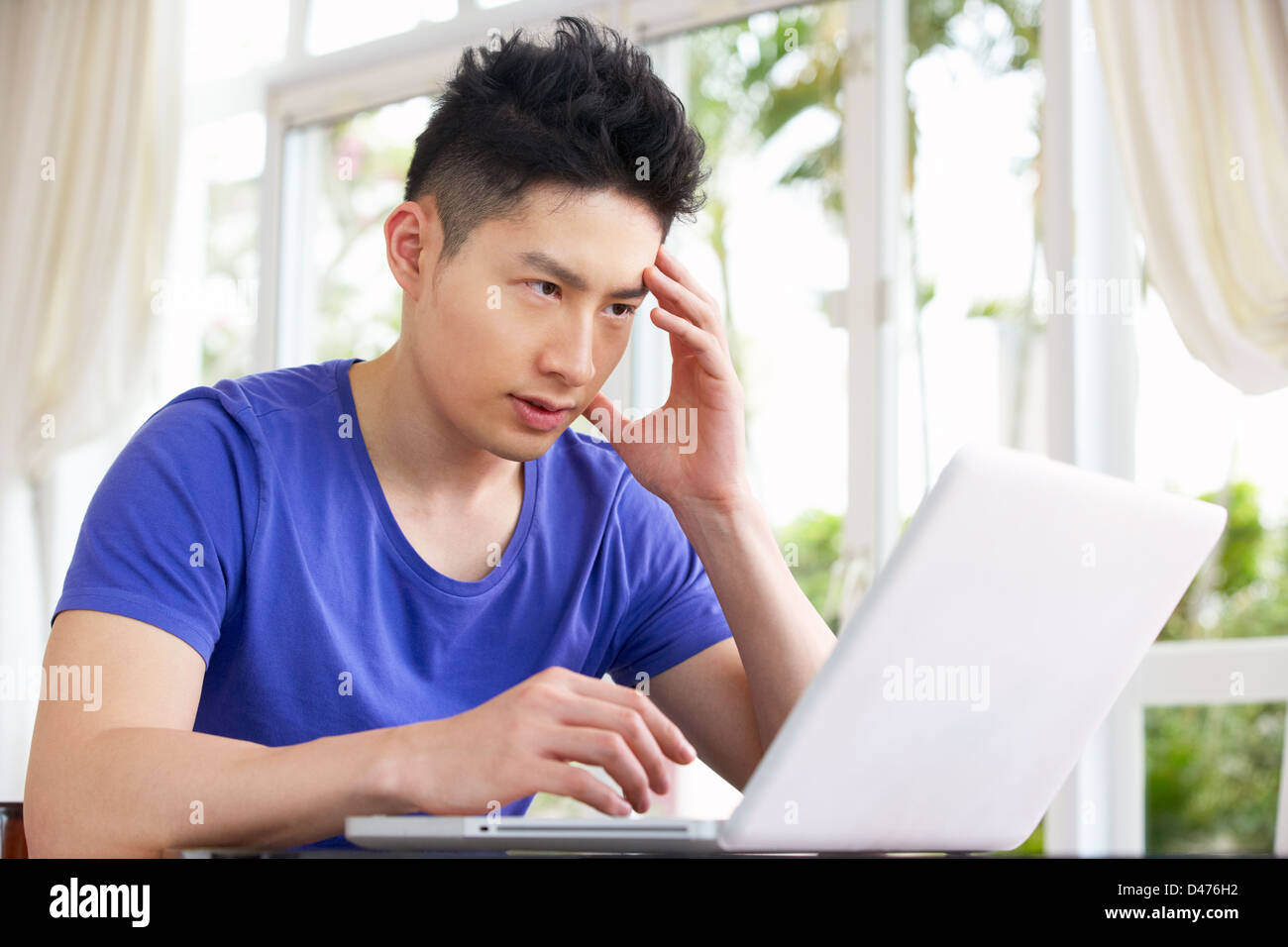 Jungen chinesische Mann am Schreibtisch mit Laptop zu Hause besorgt Stockfoto