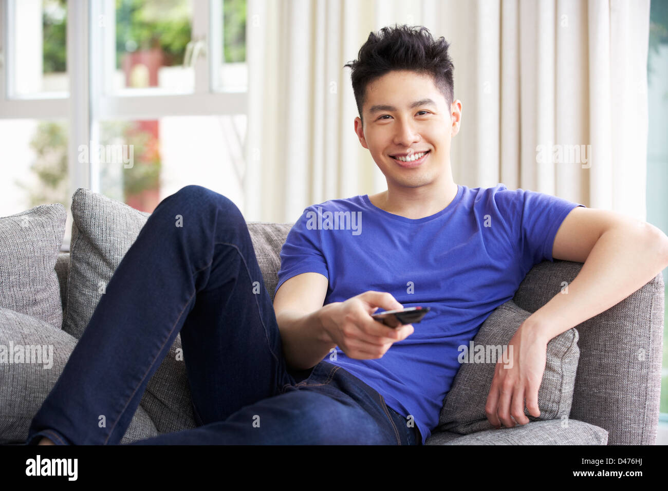 Junge Chinesen Mann zu sitzen und zu Hause vor dem Fernseher auf Sofa Stockfoto